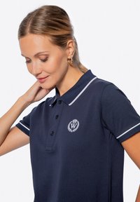 Polo shirt navy con accenti bianchi, caratterizzato da maniche corte, colletto, patta con tre bottoni e un emblema ricamato sul petto.