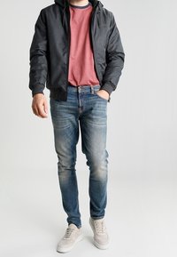 Svart huvjacka över en röd t-shirt, i kombination med urtväädade blå jeans och ljusa sneakers. Enkel, avslappnad outfit.