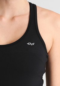 Czarny sportowy top na ramiączkach o dopasowanym kroju, wykonany z gładkiego materiału. Posiada małe białe logo po lewej stronie, blisko dekoltu.