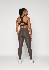 Black sports bra with racerback design, paired with high-waisted, smooth, olive-green leggings and white athletic shoes.