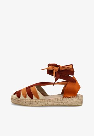 Sandalia plana tipo esparto con suela beige, tiras de tela en naranja y óxido, y cordones para el tobillo en colores a juego.