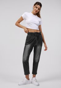 Donkergrijze joggerbroeken met een trekkoord in de taille, taps toelopende pijpen en een zachte textuur, gecombineerd met een aansluitend witte crop top en witte sneakers.