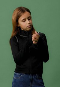 Musthave mustriga musta jakk, millel on kõrge krae ja peegeldavad detailid, kombineeritud siniste denimiste teksadega. Sile tekstuur ja sobiv disain.