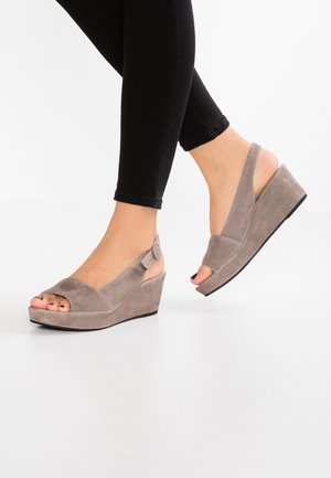 Sandales compensées en suède gris avec un bout ouvert, une bride arrière et un talon texturé, associées à un jean skinny noir.