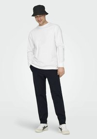 Witte lange mouwen t-shirt, zwarte bucket hat, navy broek en witte sneakers met zwarte accenten. Eenvoudig ontwerp, casual pasvorm.