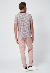 Kortärmad skjorta med ett geometriskt mönster i rött, blått och vitt. Bärs med ljusrosa byxor och vita sneakers med svarta detaljer.