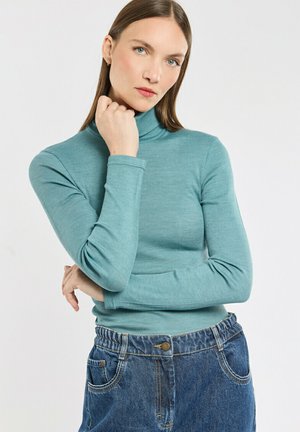 Haut en turtleneck côtelé de couleur bleu sarcelle clair avec des manches longues, associé à un jean en denim bleu taille haute et ample avec une fermeture à bouton.