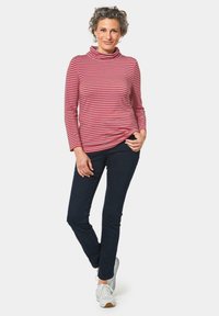 Rot- und rosa gestreifter Rollkragenpullover mit langen Ärmeln, kombiniert mit dunkelblauen Hosen und weißen Turnschuhen. Glatter Stoff mit lockerer Passform.