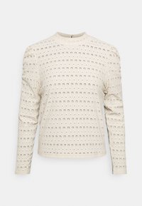 Beige long-sleeve top with a textured fabric and circular cut-out patterns. Features a round neckline and slightly puffed shoulders.