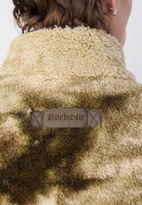 Tan en groene fleece jas met een textuur oppervlak. Beschikt over een zichtbare "Barbour" label gestikt nabij de kraag.