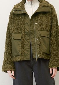 Oliven grøn jakke med en tekstureret, fluffy overflade og quiltet indre. Har trykknapper og påsyede lommer foran.