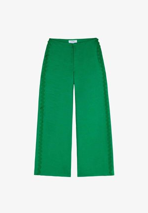 Zelené kalhoty s širokými nohavicemi vyrobené z texturované tkaniny, zdobené vykrojenými detaily podél bočních švů a uvolněným střihem.