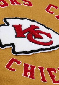 Kansas City Chiefs logo in red and white on a mustard yellow fabric background with partially visible red text.