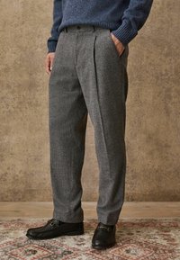 Gray textured trousers with front pleats and pockets, paired with black shoes featuring a buckle accent. Casual sweater visible at the top.