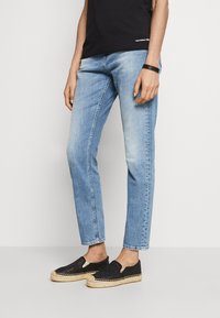 Jeans en denim bleu clair avec une coupe droite et un léger délavage, associées à des chaussures noires à enfiler avec un design tissé et une semelle en jute.