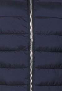 Navy Pufferjacke mit horizontalem Steppdesign, metallischem Reißverschluss und glatter Textur. Geeignet für kaltes Wetter.