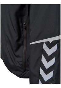 Gros plan sur une veste noire avec une poche zippée et un motif en chevron réfléchissant sur la manche pour la visibilité.