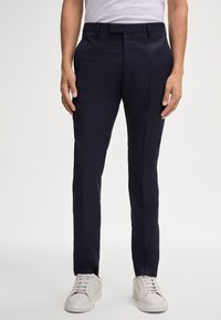 Marineblaue, maßgeschneiderte Hosen mit glatter Textur, flacher Vorderseite und dezenten Nahtdetails, kombiniert mit weißen Sneakers.