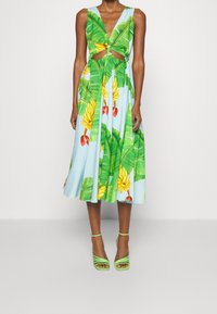 Blomsterkjole med blå baggrund, prydet med grønne bananblade og frugttryk, med udskåret talje og en udskåret skirt; parret med grønne hæl-sandaler.