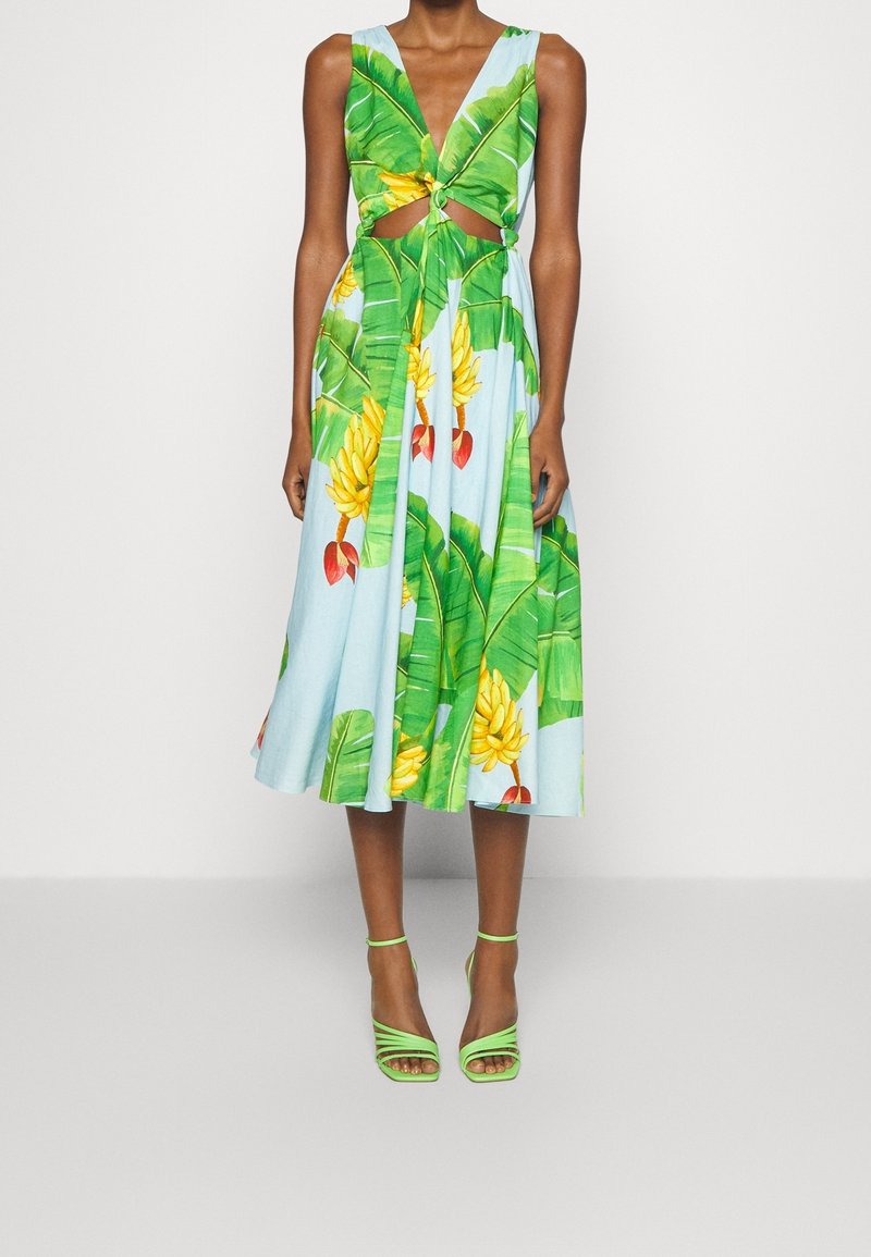 Blomsterkjole med blå baggrund, prydet med grønne bananblade og frugttryk, med udskåret talje og en udskåret skirt; parret med grønne hæl-sandaler.