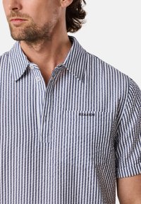 Camicia a maniche corte con strisce verticali blu e bianche, patta dei bottoni, e una tasca sul petto sinistro con ricamo "SEASIDE".