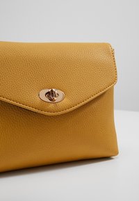 Clutch gialla in pelle con finitura testurizzata, dotata di chiusura magnetica arrotondata e design della patta inclinata.