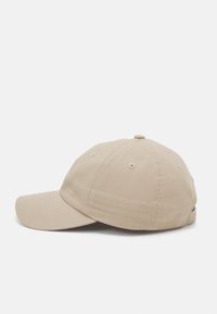 Beige baseball cap made of cotton. Features a rounded crown, a curved brim, and ventilation holes, with an adjustable strap at the back.