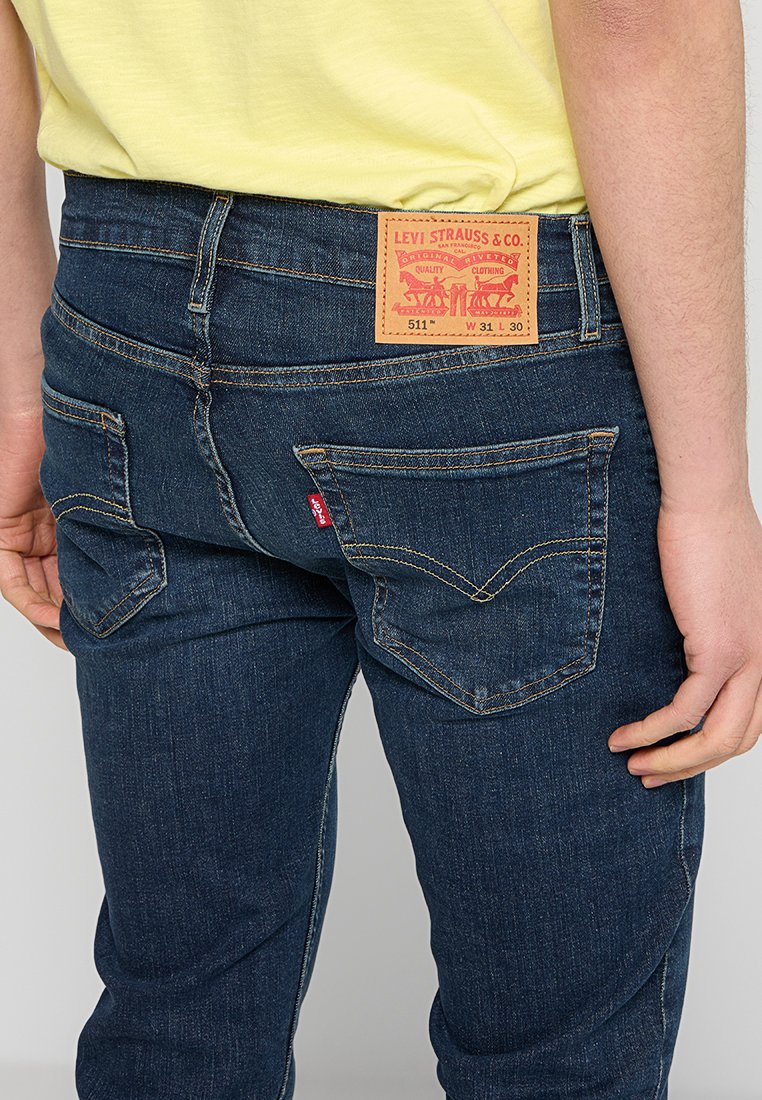 Dunkelblaue Jeans aus Denim mit schlankem Schnitt, versehen mit einem Lederpatch am hinteren Bund, das Markendetails anzeigt, sowie zwei Gesäßtaschen.