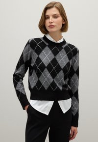 Zwarte en grijze sweater met argyle-patroon en een ronde halslijn, met ribgebreide manchetten en zoom, gedragen over een witte blouse met kraag.