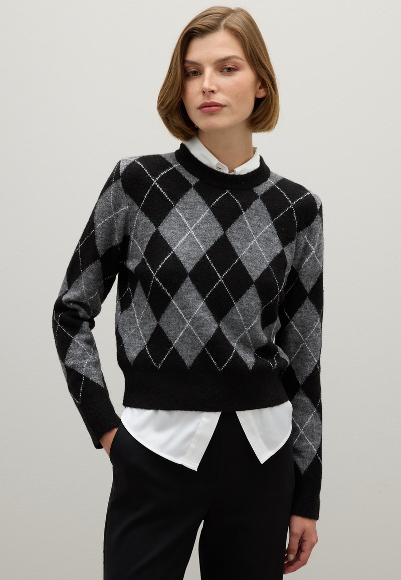 Zwarte en grijze sweater met argyle-patroon en een ronde halslijn, met ribgebreide manchetten en zoom, gedragen over een witte blouse met kraag.