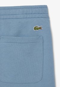 Pantalones de chándal de algodón azul con un bolsillo trasero y un logo de cocodrilo verde bordado. Textura suave y cintura elástica estándar.