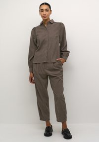 Brown, textured shirt with a collar and button-front, paired with matching loose-fit trousers. Black slip-on shoes complete the outfit.