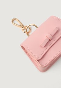 Porte-clés en cuir rose avec détail en nœud et anneau en métal doré, sur un fond blanc.