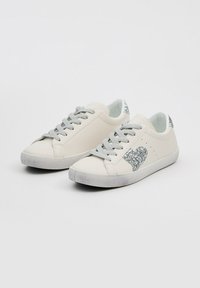 Zapatillas blancas con cordones grises y un acento de corazón brillante. Material de cuero suave, punta redondeada y suela de goma texturizada.