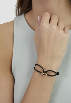 Black cord bracelet featuring a gold ring centerpiece, showcasing a knotted design against a light gray background.