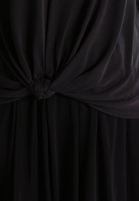 Svart klänning med en knutdetalj vid midjan, tillverkad av mjukt, fallande tyg med en slät yta och flödande silhuett.