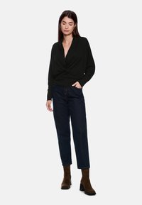 Schwarzes, langärmliges Wickeloberteil mit tiefem Ausschnitt; kombiniert mit dunkelblauen, leicht locker sitzenden Jeans und braunen Wildleder-Stiefeletten.