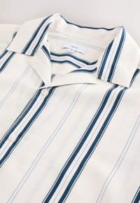 Chemise à manches courtes avec des rayures verticales bleu marine et bleu clair sur fond crème, dotée d'un col boutonné et fabriquée en coton doux.