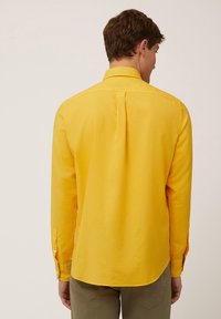 Camisa de manga larga, abotonada, en un brillante color amarillo, hecha de algodón, con un pliegue en la parte posterior y puños abotonados. Diseñada con un dobladillo curvado.
