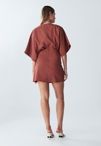 Kratka haljina od rđe s opuštenim krojem, kimono rukavima i zatvaranjem na leđima. Glatka tkanina s laganim sjajem. Jednostavan dizajn.