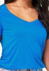 Blå v-hals t-shirt med korte ærmer, glat tekstur og minimale sømme, parret med lyse denimshorts.