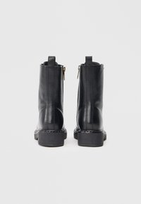 Botine negre din piele cu o textură netedă, având un fermoar lateral, vârf rotund și un toc mic cu talpă cusută.