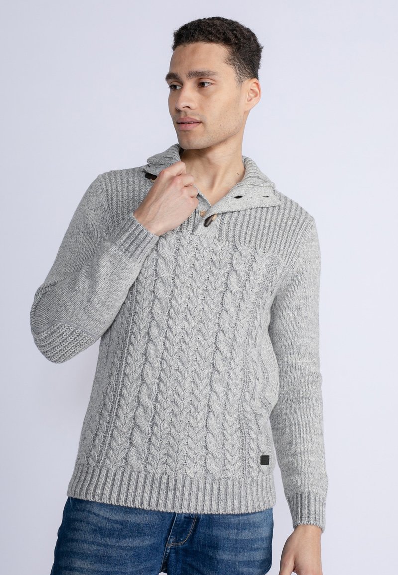 Pulover gri tricotat cu guler tip șal, butoni din lemn, manșete și tiv cu aspect rasucit. Purtați-l cu blugi albaștri, punând în evidență textura și detaliile de design.
