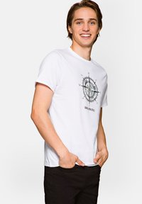 Biała bawełniana koszulka z grafiką kompasu w odcieniach szarości, krótki rękaw, okrągły dekolt, w zestawie z czarnymi spodniami.