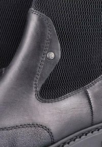 Melnas ādas potītes zābakus ar teksturētu sietu paneļu, kura kreisajā pusē ir sudraba dekoratīva pogas un kontrastējoša dūriena.