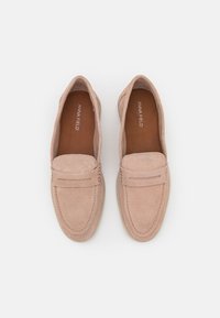 Un paio di mocassini slip-on in suede beige con dettagli di cucitura e brand "Anna Field" all'interno, mostrati dall'alto su uno sfondo bianco.