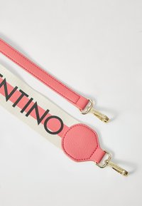 Rosa läderrem med ett beige tygstycke som har "VALENTINO" i fet svart text och guldackenter. Texturerad yta är synlig.