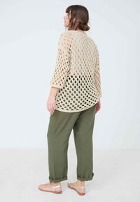 Haut en crochet beige avec des motifs circulaires ouverts, manches trois quarts, associé à un pantalon olive retroussé et des sandales marron.