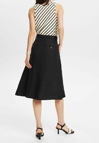 Falda negra en línea A con una cintura ajustada, que presenta bolsillos traseros y una textura suave, combinada con un top sin mangas a rayas y tacones negros.
