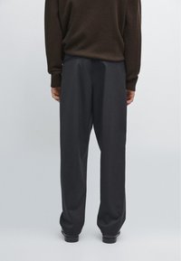  Sorte bukser med løs pasform, der har en glat tekstur og minimalistisk design. Taljen er lidt højt placeret for komfort.